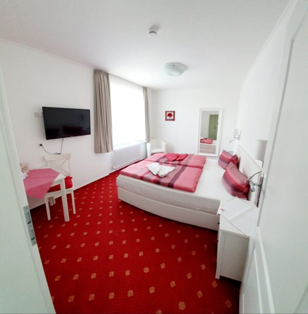 Cozy double room at Haus Hubertus on Borkum with a comfortable bed, red carpet, flat-screen TV, and bright, inviting decor for a relaxing stay.