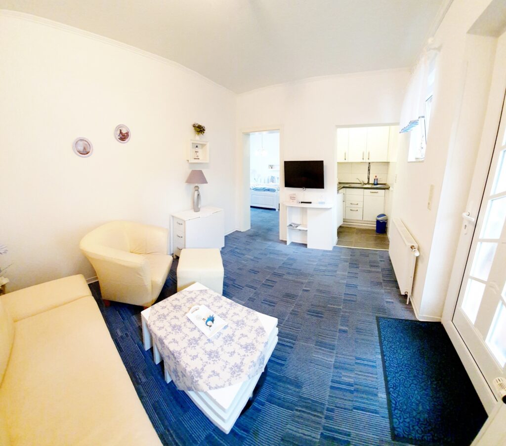 Helles Wohnzimmer in einer Ferienwohnung im Haus Hubertus auf Borkum mit gemütlicher Sitzecke, TV und offener Küchenzeile für einen entspannten Urlaub.