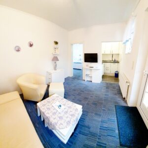 Helles Wohnzimmer in einer Ferienwohnung im Haus Hubertus auf Borkum mit gemütlicher Sitzecke, TV und offener Küchenzeile für einen entspannten Urlaub.