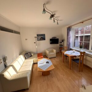 Helles Wohnzimmer im Haus Hubertus auf Borkum mit gemütlichem Sofa, Essbereich, Flachbildfernseher und hellem Parkettboden für einen entspannten Urlaub.