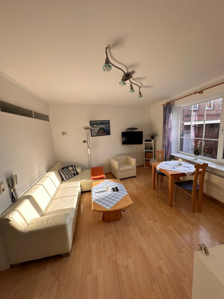 Helles Wohnzimmer im Haus Hubertus auf Borkum mit gemütlichem Sofa, Essbereich, Flachbildfernseher und hellem Parkettboden für einen entspannten Urlaub.