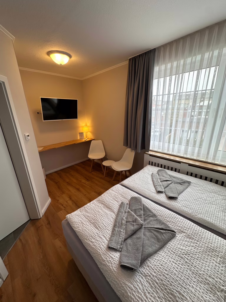 Cozy Doppelzimmer Komfort at Haus Hubertus on Borkum, featuring two single beds with grey towels, modern furniture, and a bright, inviting atmosphere.