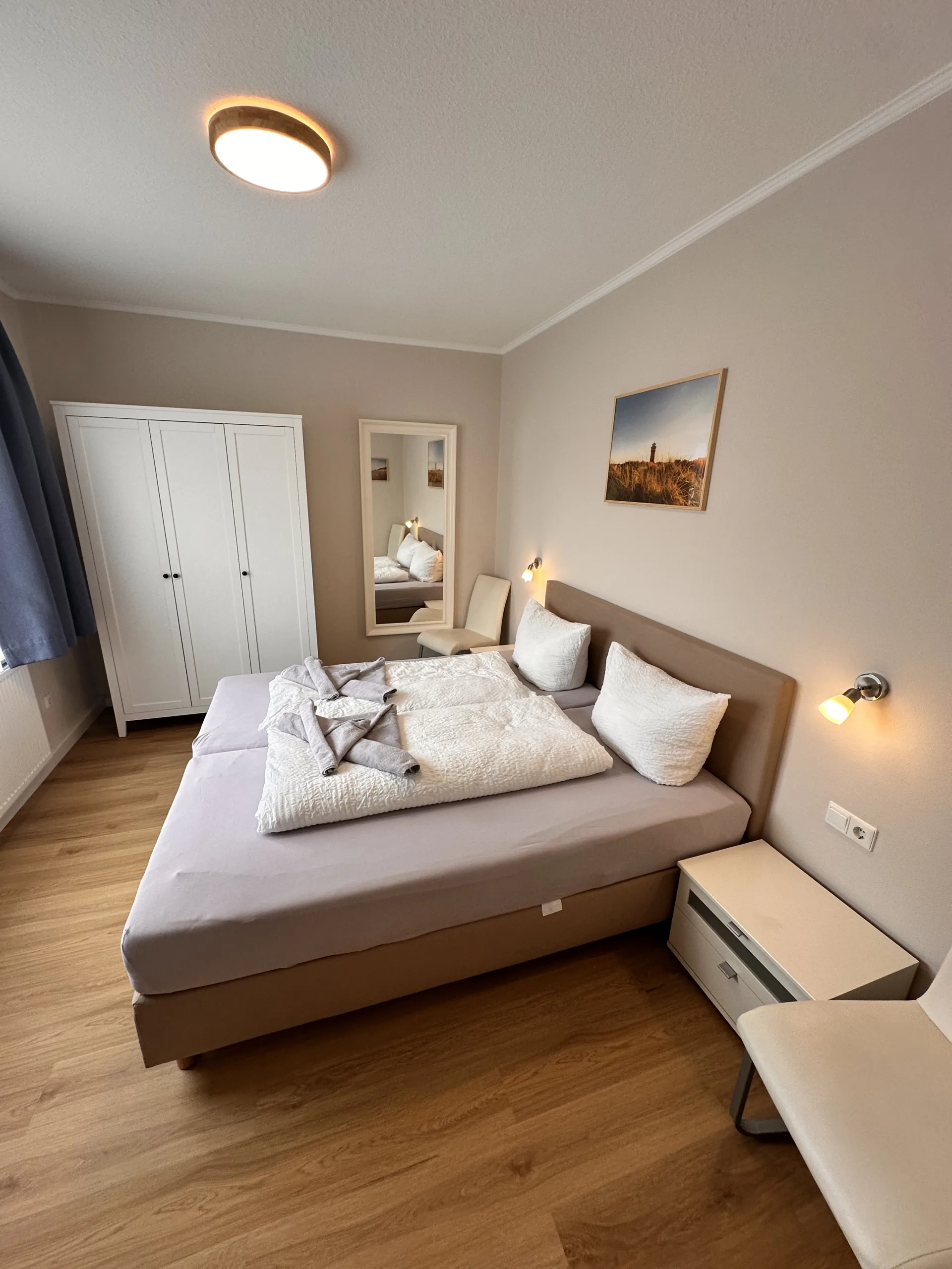Cozy bedroom at Haus Hubertus on Borkum with a comfortable double bed, white wardrobe, wooden flooring, and a relaxing, modern interior design.