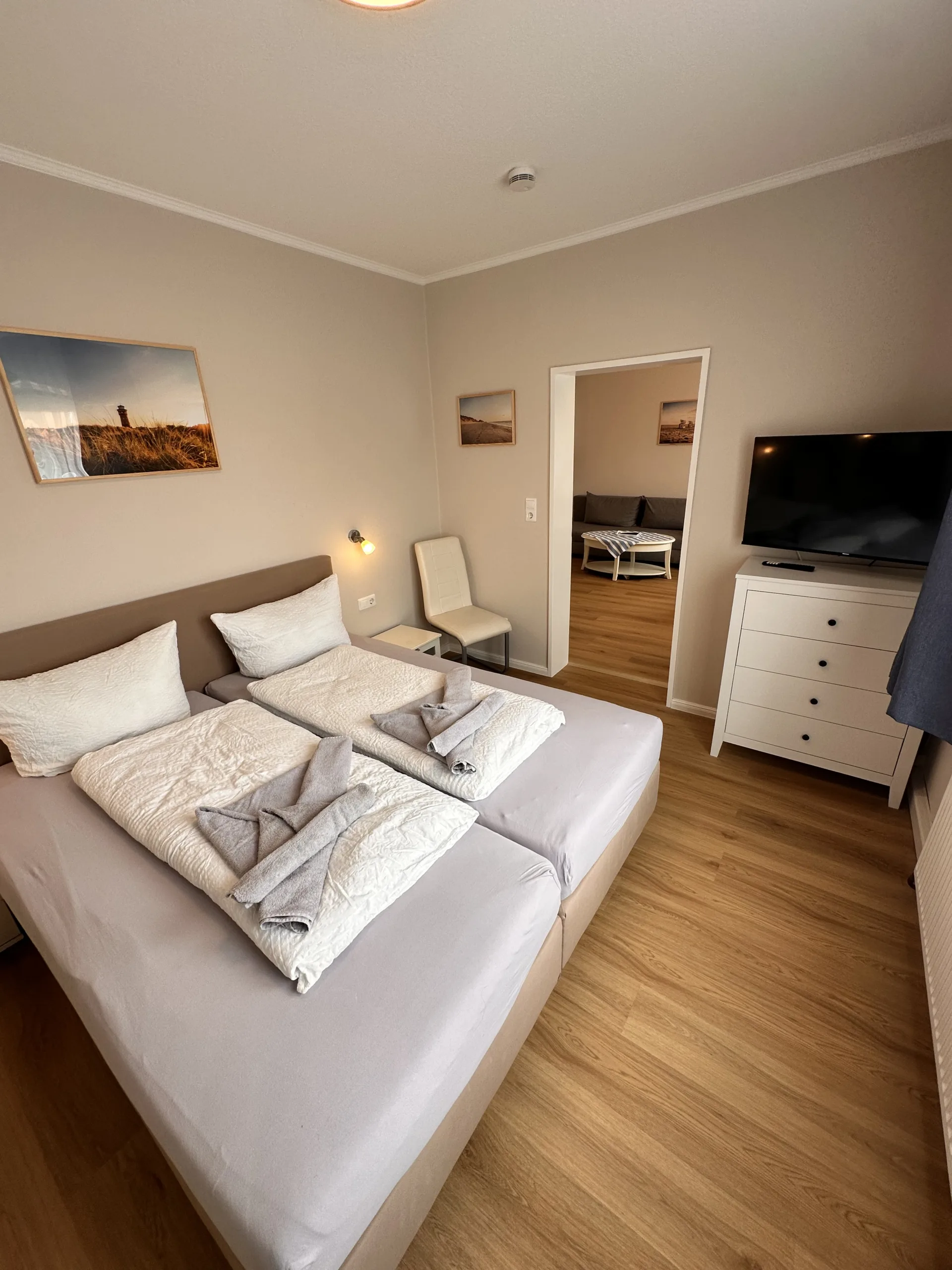 Cozy bedroom at Haus Hubertus on Borkum with a double bed, white dresser, flat-screen TV, and a view into a bright, comfortable living area.
