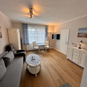Cozy living room in Haus Hubertus on Borkum featuring a comfortable sofa, dining area, flat-screen TV, and bright, inviting decor for your vacation.