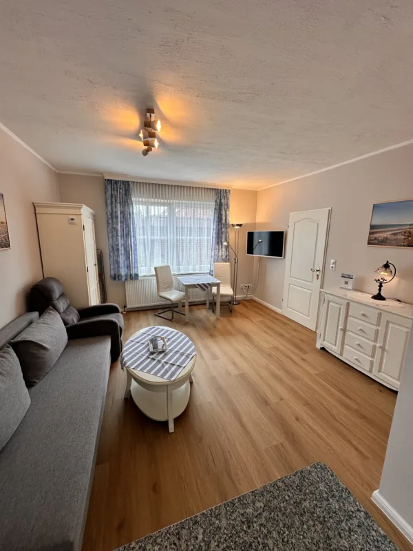 Cozy living room in Haus Hubertus on Borkum featuring a comfortable sofa, dining area, flat-screen TV, and bright, inviting decor for your vacation.