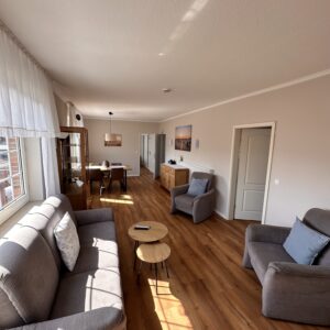 Bright, modern living room in a Hubertus holiday flat on Borkum, featuring comfortable grey sofas, wooden floors, and a cozy dining area.